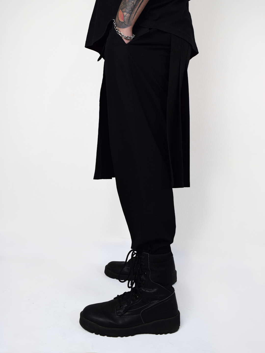 Sobrecapa tipo kilt negro industrial utilizada sobre pantalón estilo streetwear alternativo